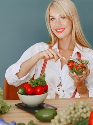Blonde woman enjoying a fresh salad surrounded by vegetables, promoting healthy eating.