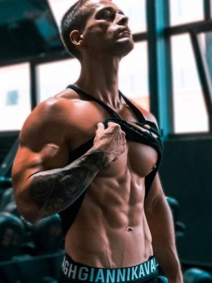 Muscular man showing abs and tattoos in a gym setting.